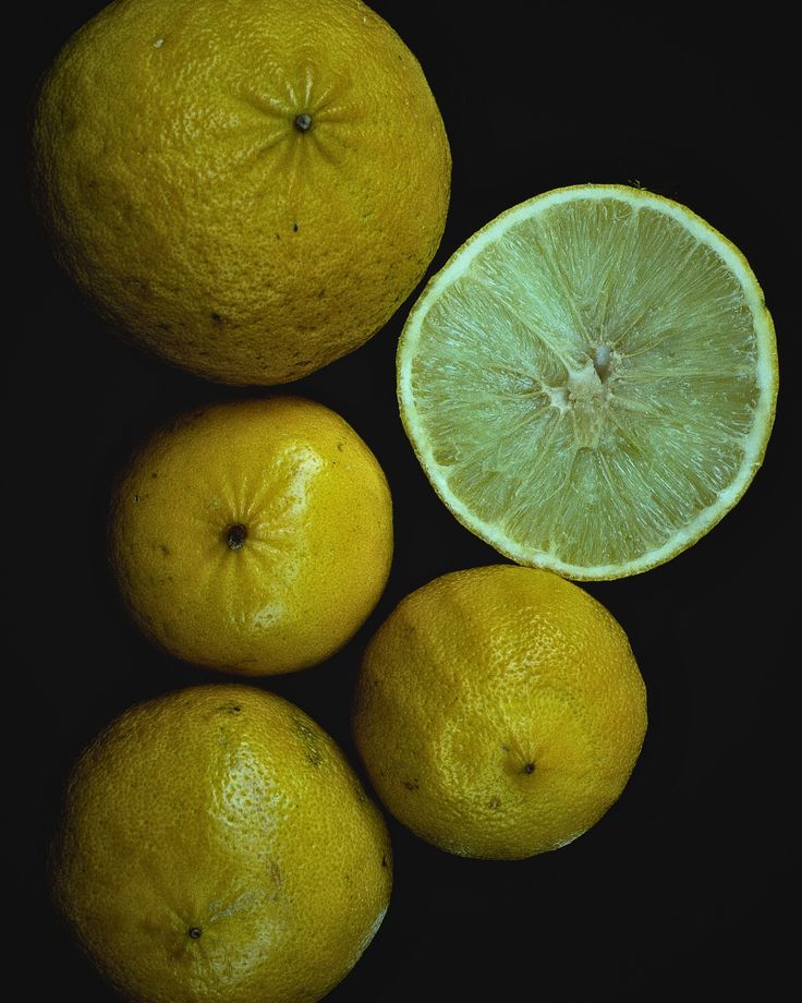 three lemons with one cut in half and the other whole on a black background