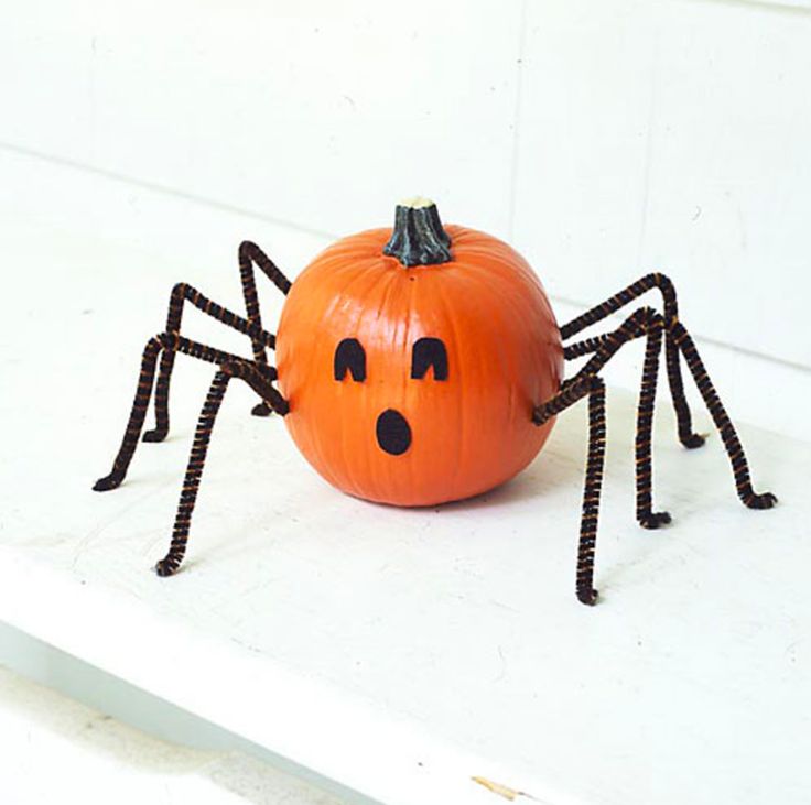 a pumpkin decorated like a spider sitting on top of a white shelf with its eyes open