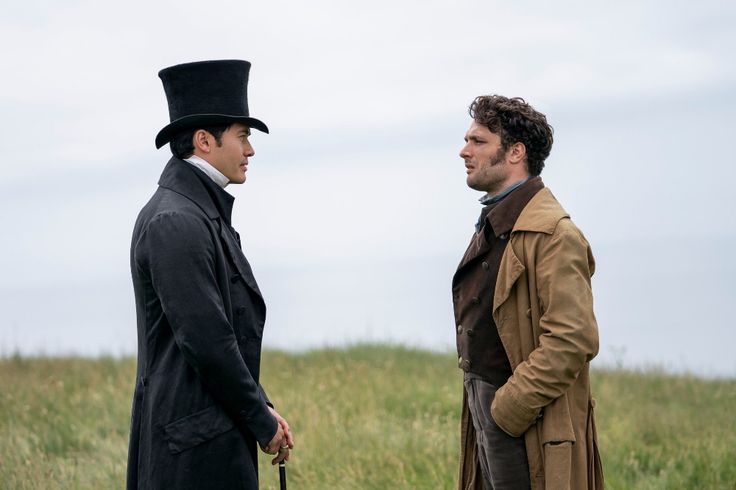 two men standing next to each other in a field with tall grass and one wearing a top hat