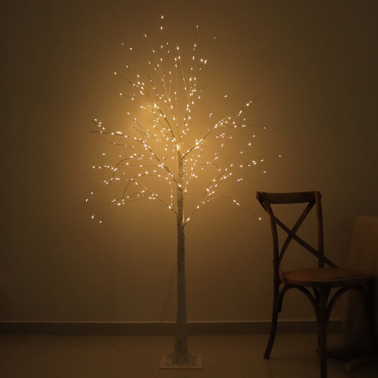 a chair sitting next to a tree with lights on it's branches in front of a wall