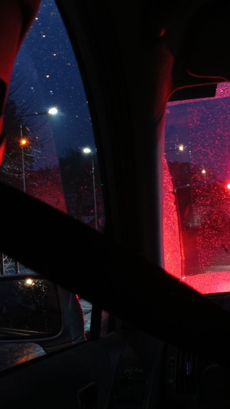 the view from inside a car at night with red lights shining on the windshield and street lamps