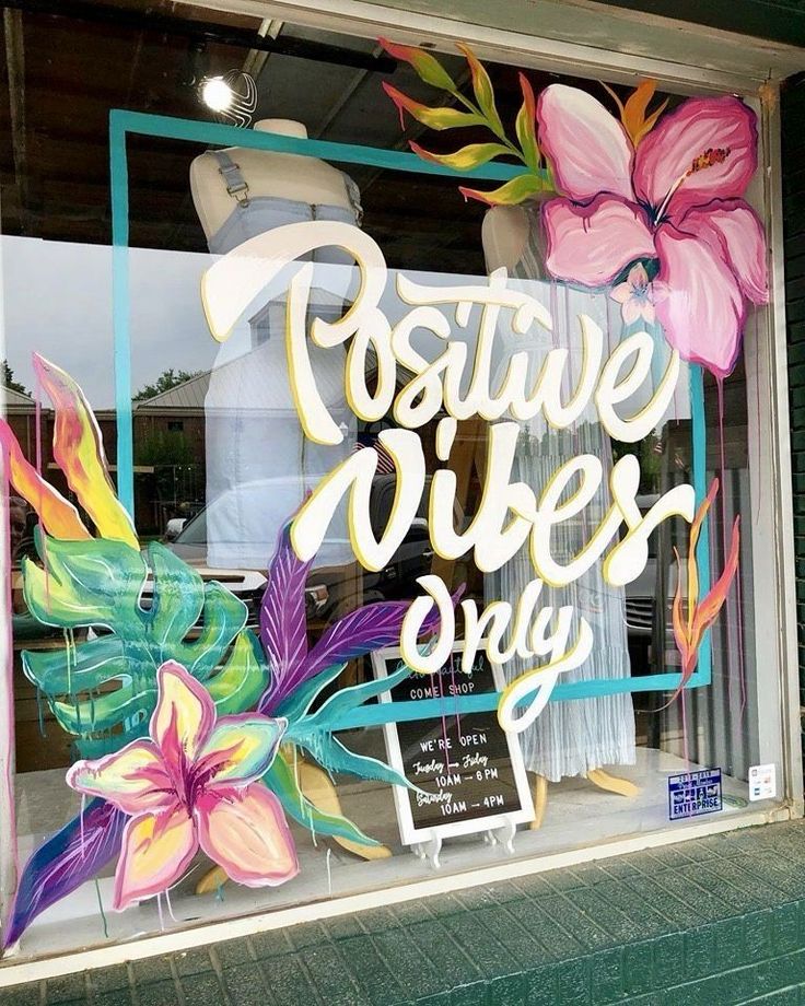 a store window with flowers painted on the glass and writing positive vibes only inside