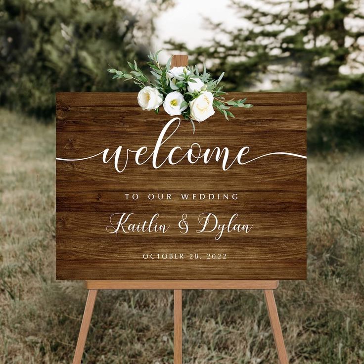 a wooden welcome sign with white flowers on it in the middle of a grassy field