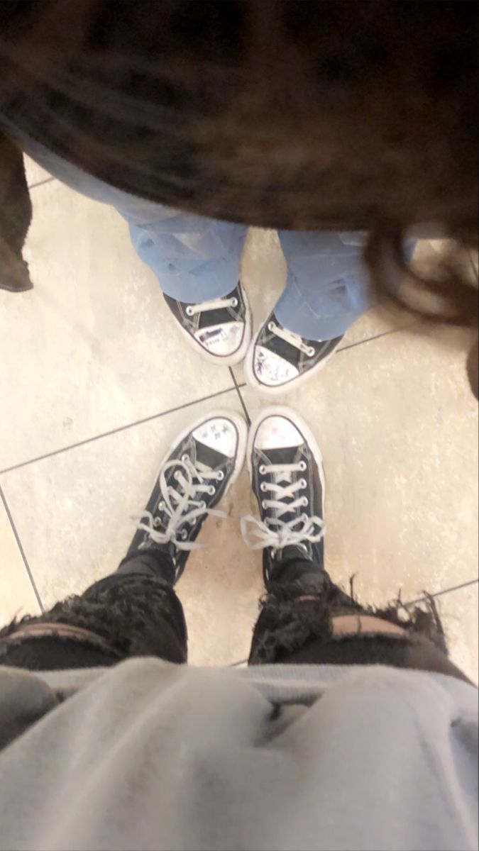 the bottom view of someone's feet standing on a tile floor with white and black shoes