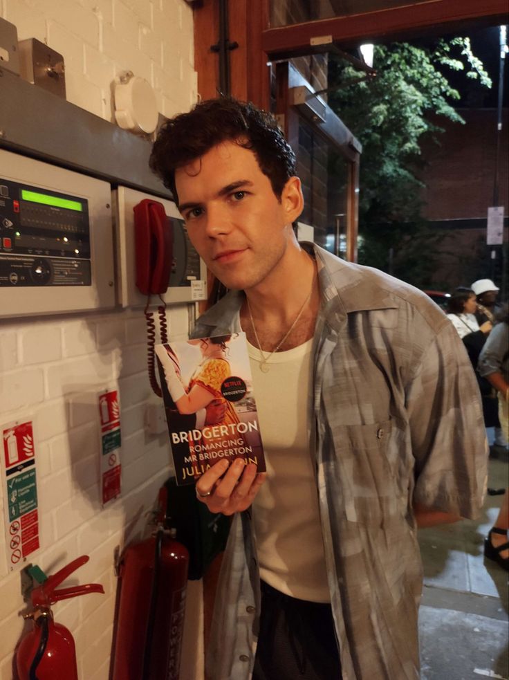 a man standing next to a red fire hydrant holding a book in his hand