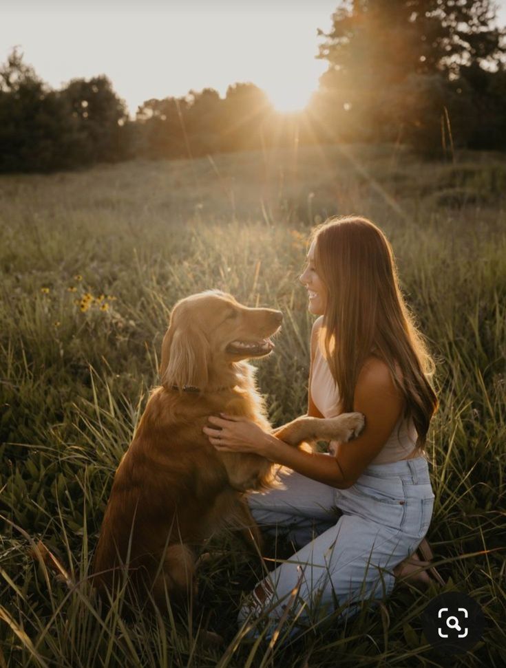 a woman is sitting in the grass with her golden retriever, who is looking into the distance