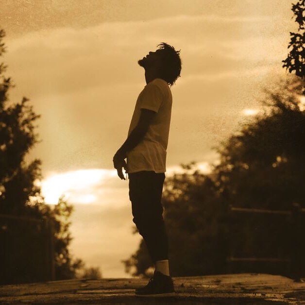 a young man standing on top of a skateboard in the street at sunset or dawn