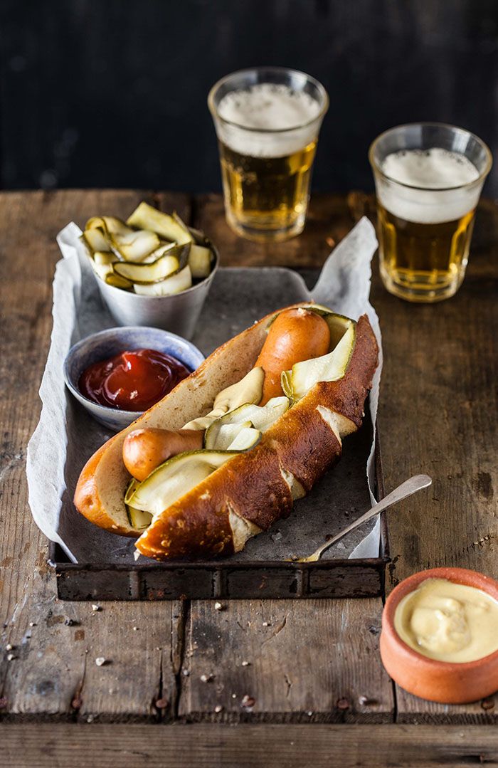 a hot dog on a bun with pickles and ketchup next to some beer