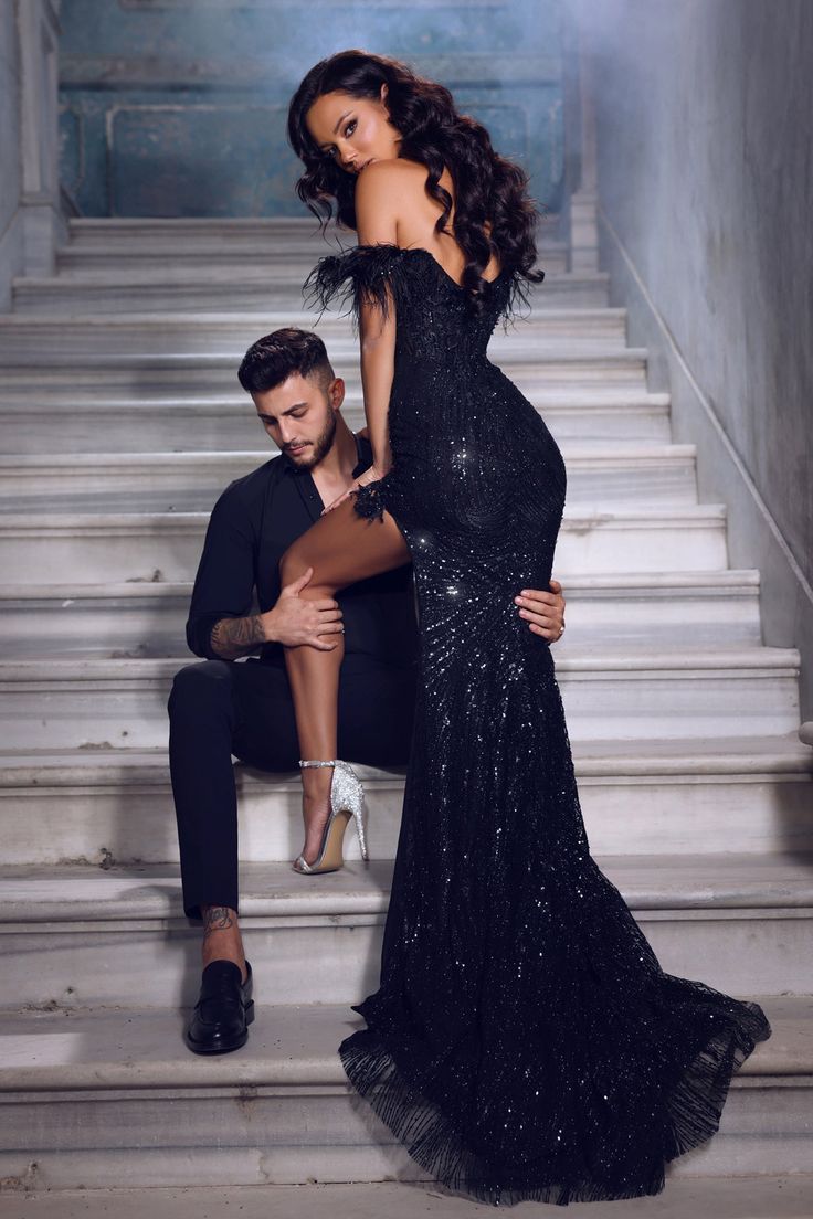 a man kneeling down next to a woman in a black dress on some stairs with their legs crossed