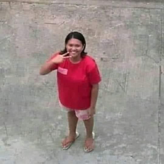 a woman standing in front of a cement wall talking on a cell phone with her hand up to her ear