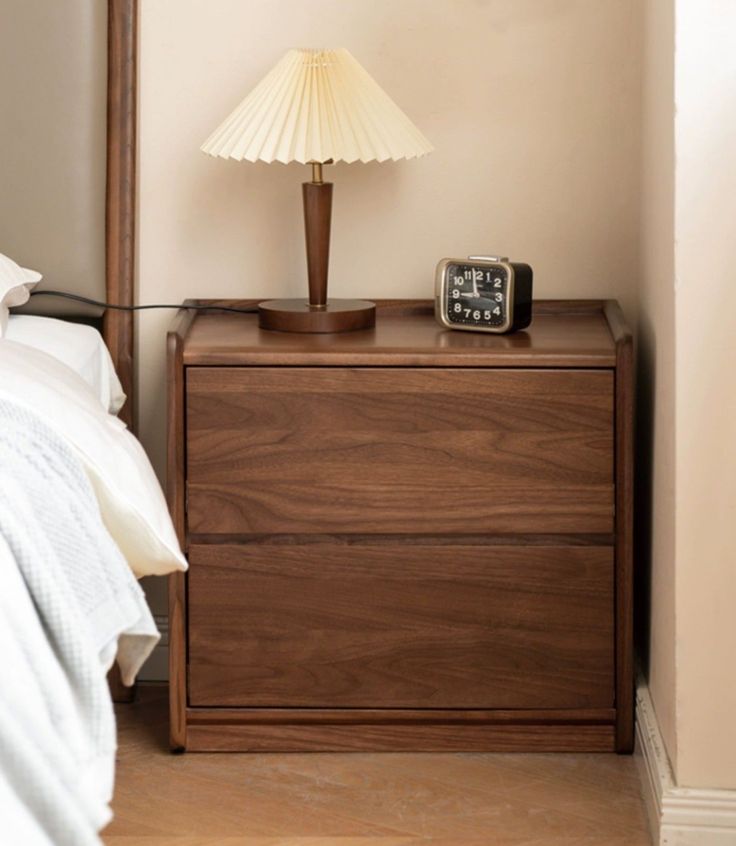 a night stand with a lamp on top of it next to a wooden dresser and bed