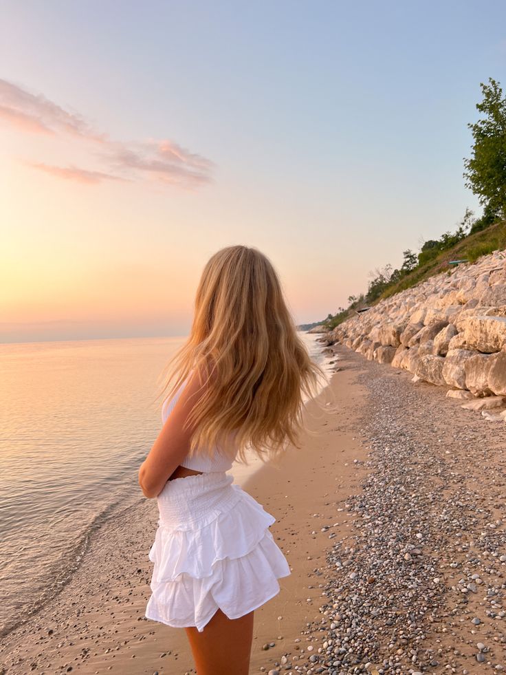 a woman standing on top of a sandy beach next to the ocean with her hair blowing in the wind