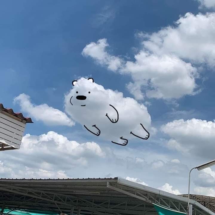 there is a kite shaped like a bear flying in the sky with clouds above it