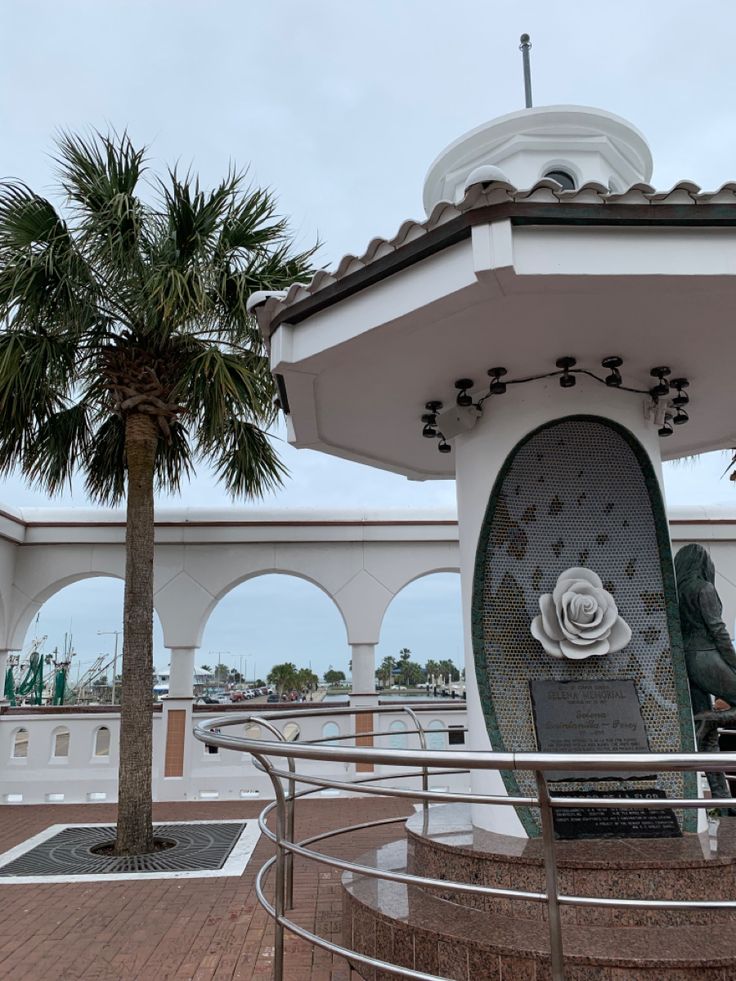 there is a statue in the center of this area with palm trees around it and a white building behind it