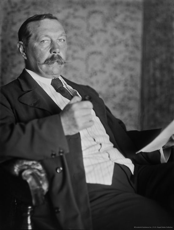 an old photo of a man in a suit and tie reading a paper while sitting on a chair