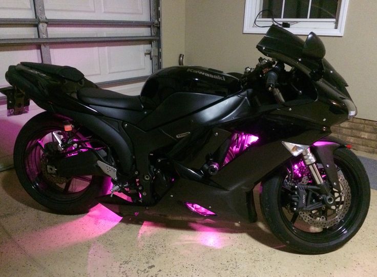 a black motorcycle parked in front of a garage with purple lights on it's side