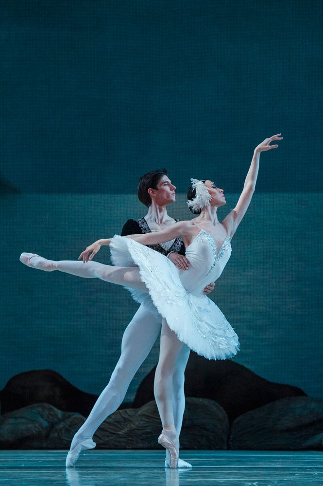 two ballerinas in white tutus and black leotards, one holding the other's leg