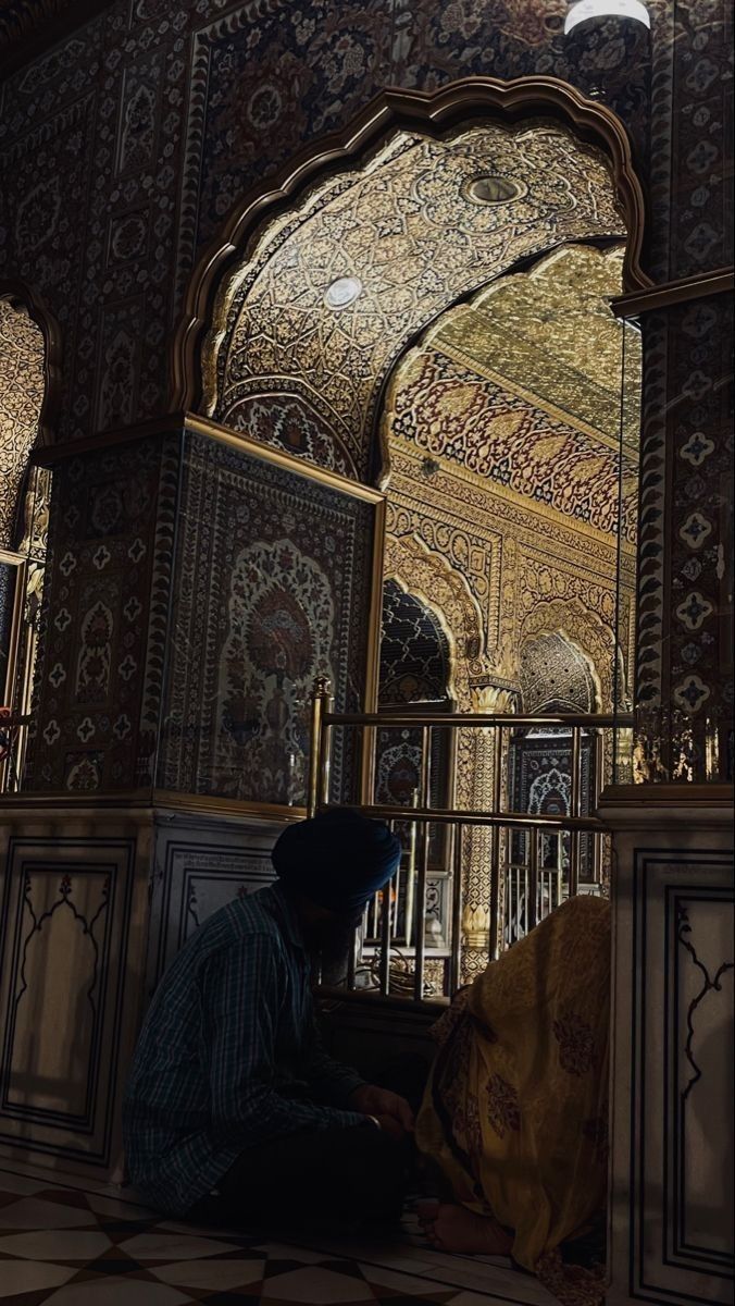 a man sitting on the ground in front of an ornate building with gold and black tiles