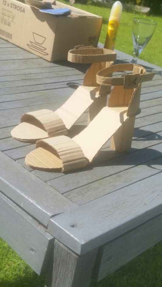 a pair of cardboard shoes sitting on top of a wooden table in front of wine glasses