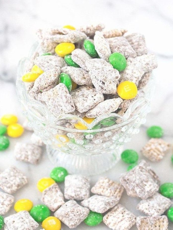 a glass bowl filled with green, yellow and white puppy chows next to candy candies