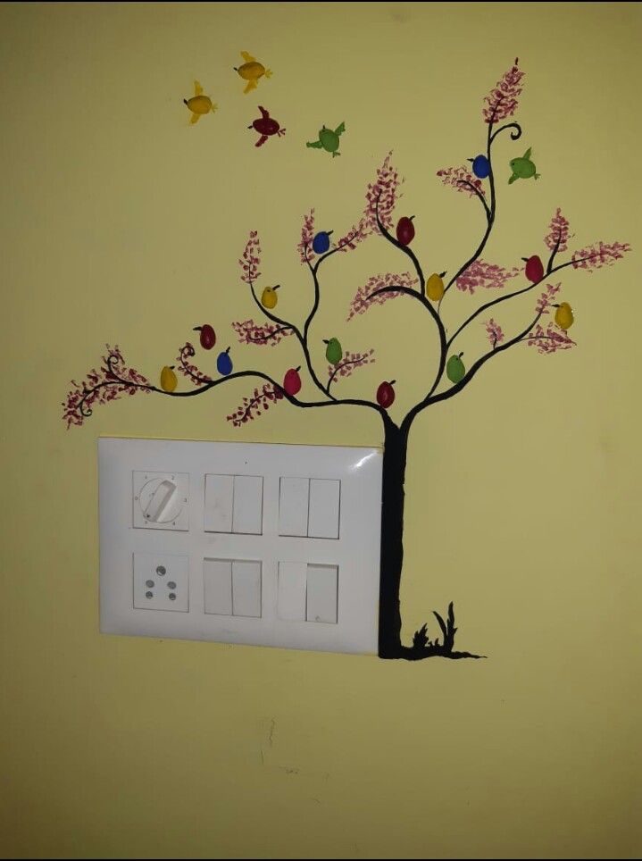 a tree with colorful leaves and birds painted on the wall next to a light switch