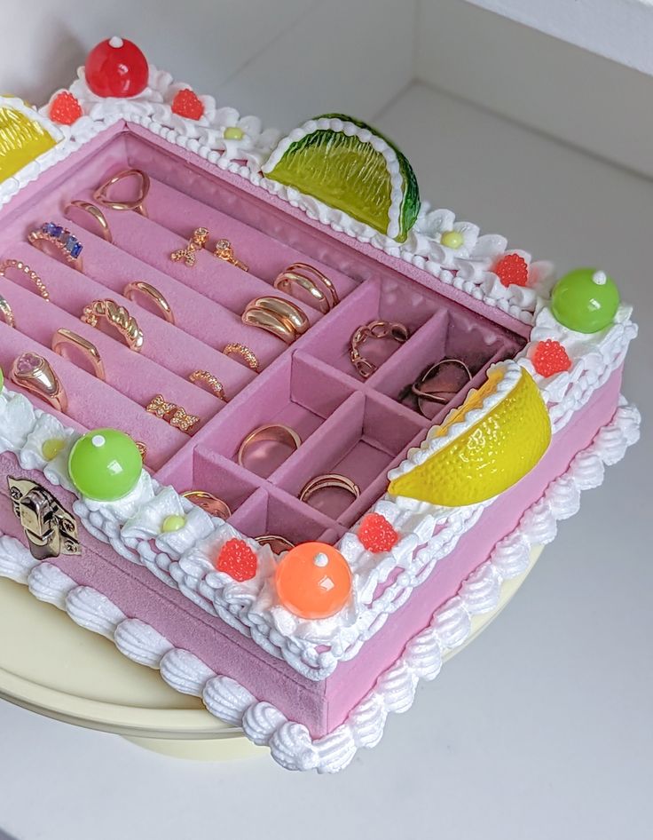 a birthday cake decorated with jewelry and fruit on the top, including an assortment of rings