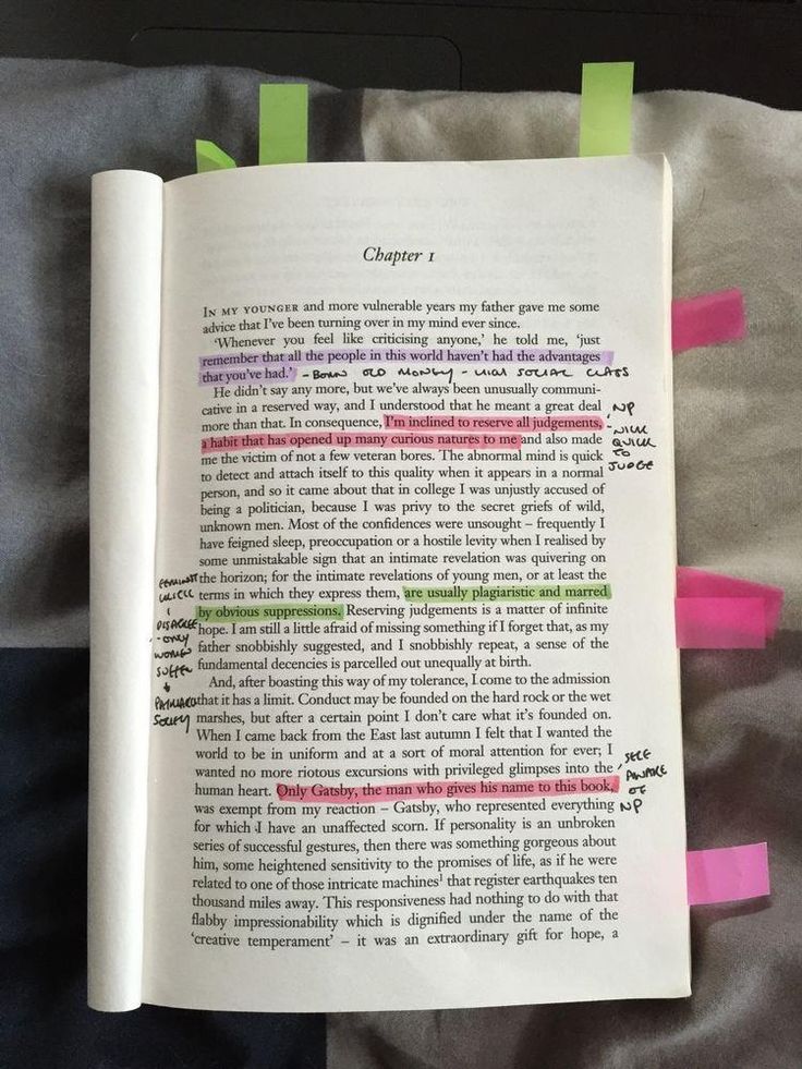 an open book with pink and green sticky notes attached to the pages, sitting on a bed