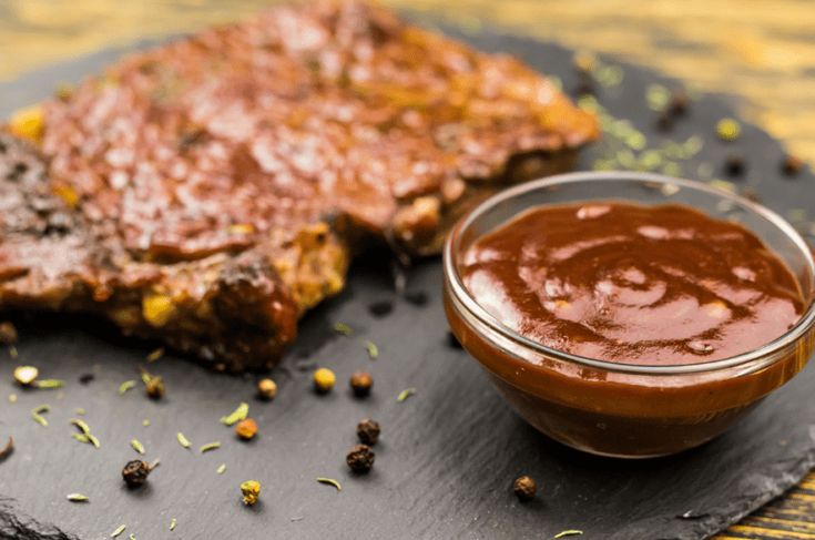 two pieces of steak on a black plate with ketchup and mustard next to it