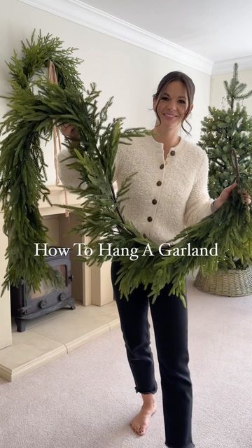 a woman standing in a living room holding two wreaths