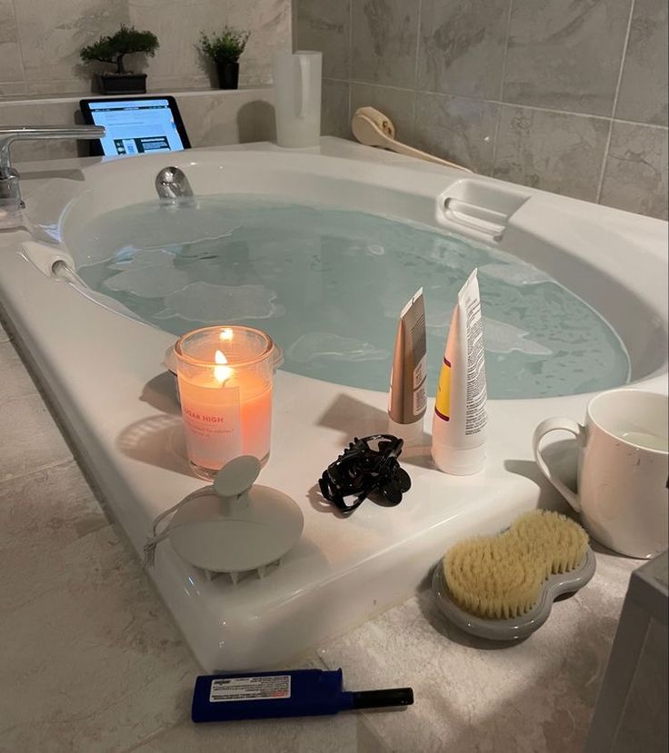 a bathtub with candles, soap and other items in it next to a laptop