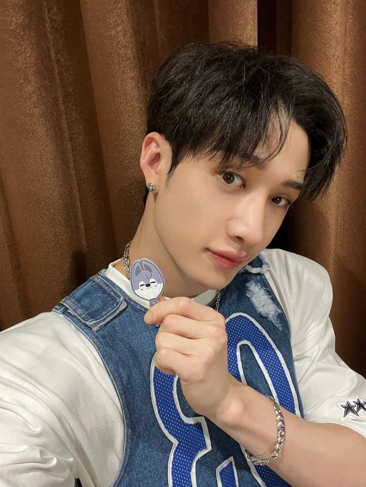 a young man wearing a denim vest and holding onto a badge