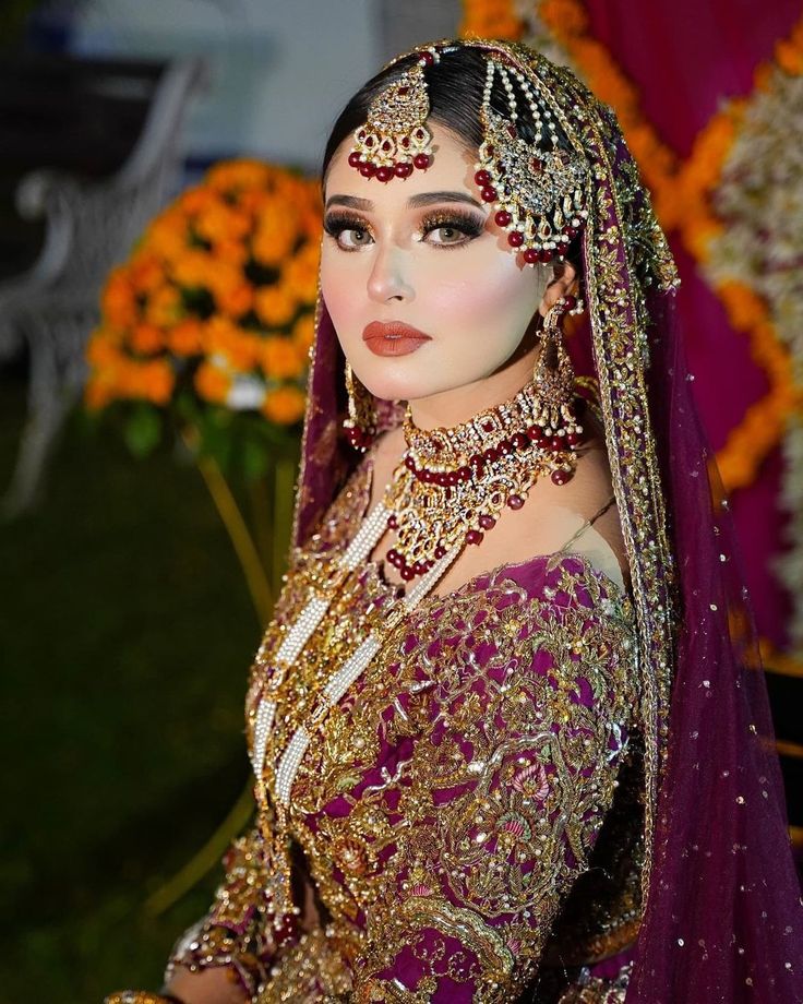 a woman in a purple and gold bridal gown with jewelry on her head, posing for the camera