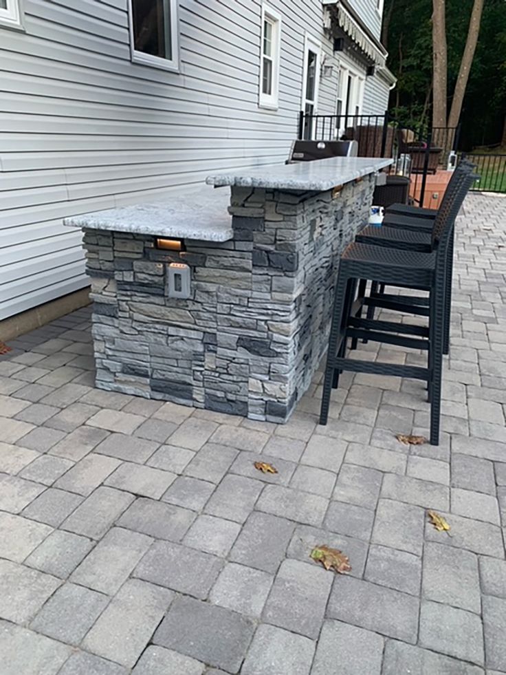 an outdoor bar with four chairs around it on a brick patio in front of a house