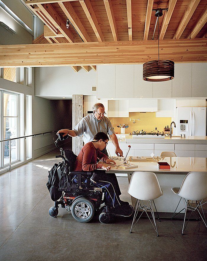 two men in wheelchairs looking at something on the kitchen table with another man standing behind them