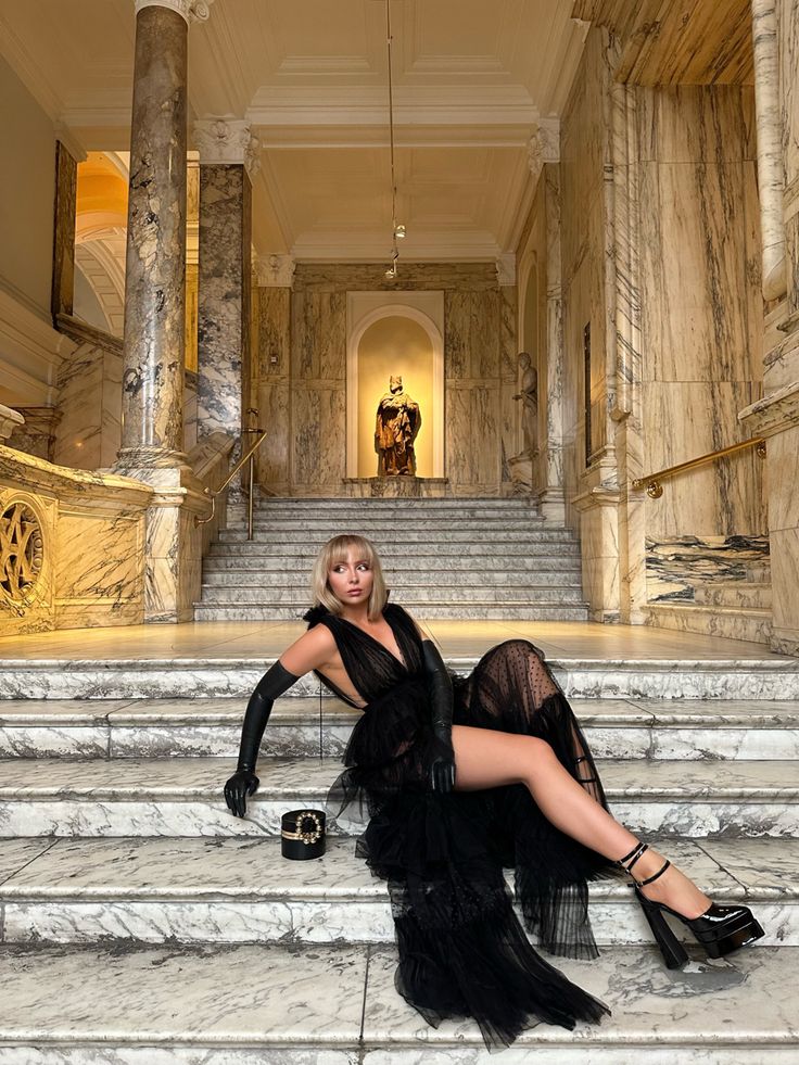 Girl laying on the steps in the Victoria and Albert museum. She is wearing a full length black dress for a special occasion. She has paired this with latex gloves and 6 inch high platform heels. She has long blonde hair and a full fringe which has been pushed behind her shoulders. Full Fringe Long Hair, Black Prom Dress Long, Full Length Black Dress, High Platform Heels, Event Dresses Long, Prom Dresses Long Black, Full Fringe, Dress Event, Girls Special Occasion Dresses