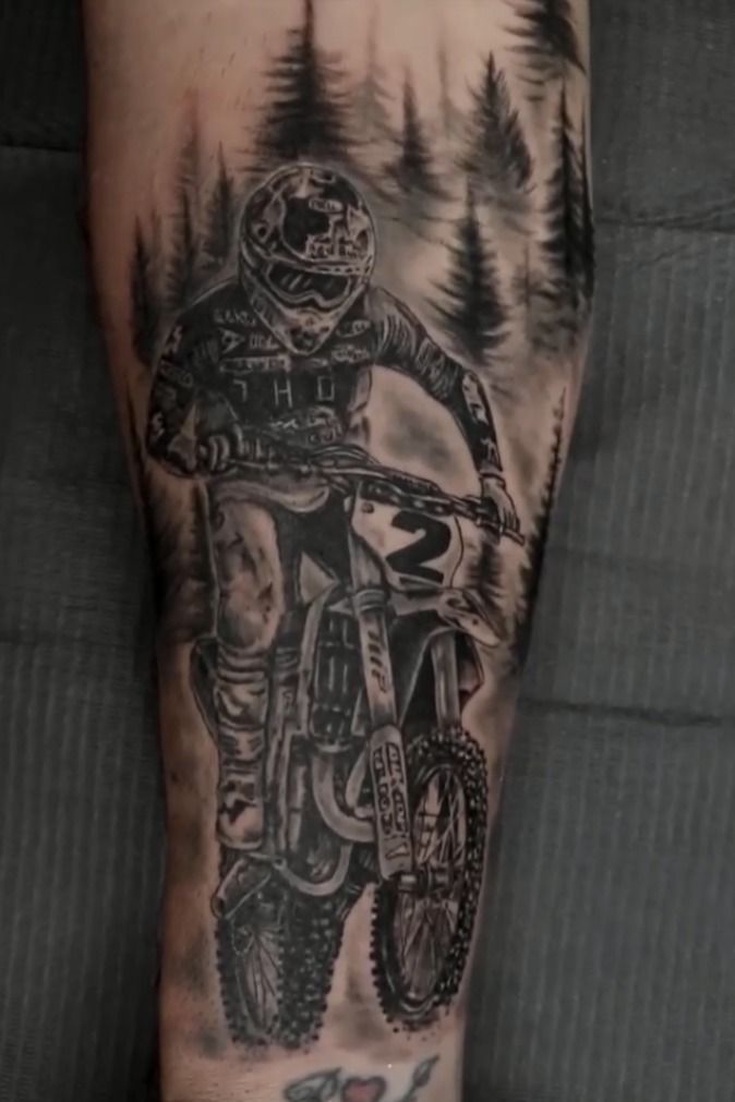 a man's leg with a tattoo of a dirt bike rider and trees on it