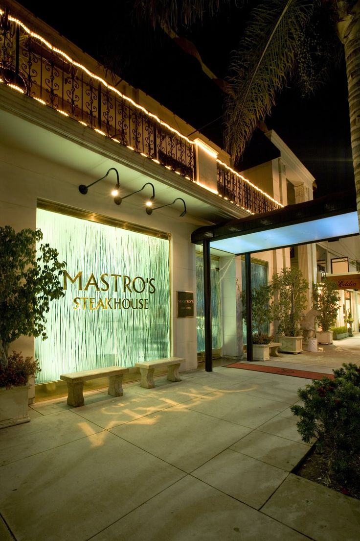 the entrance to maisto's steak house at night with palm trees in front