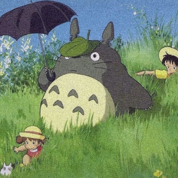 some people are in the grass with an umbrella and totoro is laying down