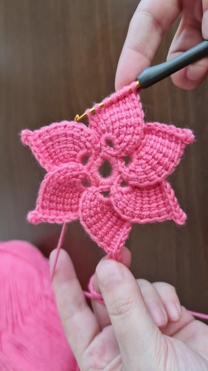 someone is crocheting a pink flower on a piece of yarn with a needle