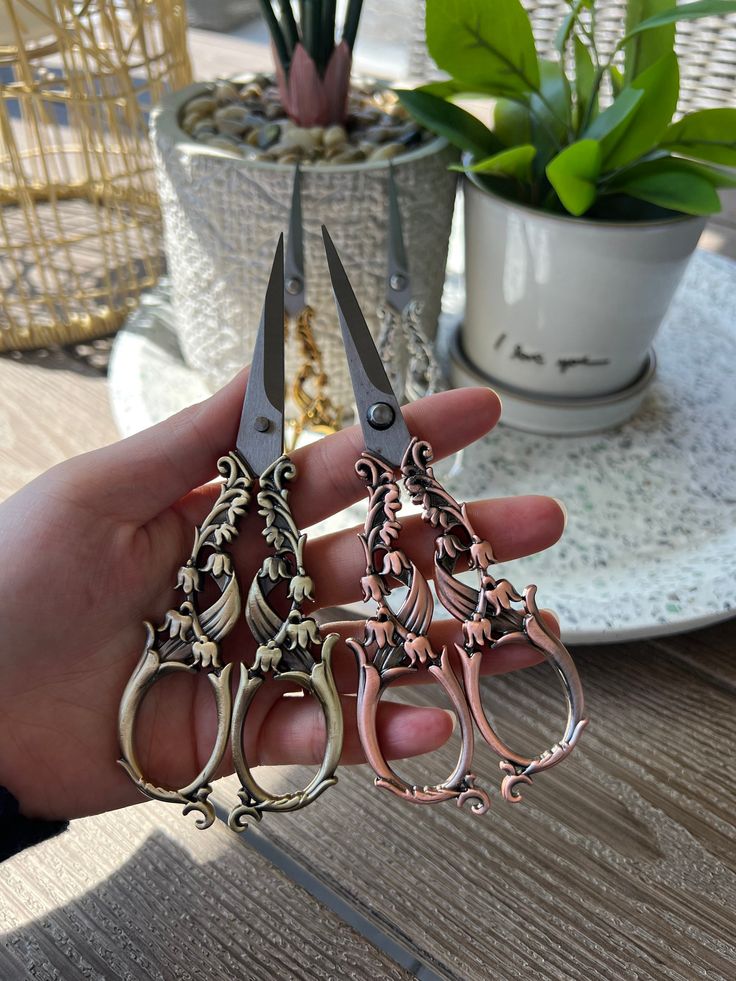 a person holding three pairs of scissors in their hand next to a potted plant