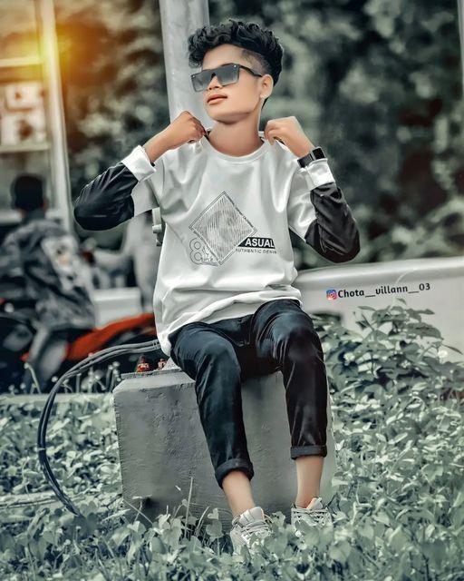 a young boy sitting on top of a cement block wearing sunglasses and a t - shirt