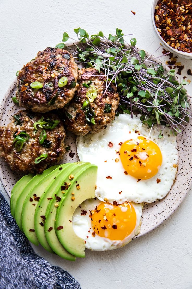 an egg, avocado and meat patties are on a plate with sprouts