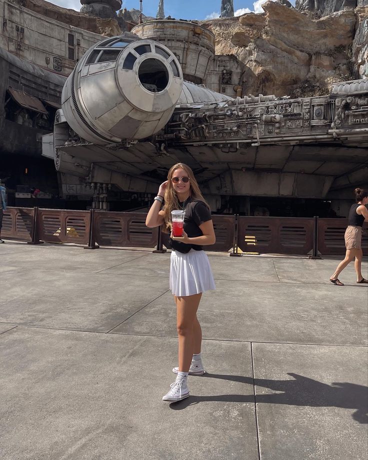 a woman is standing in front of a star wars millennium at disneyland world, holding a drink