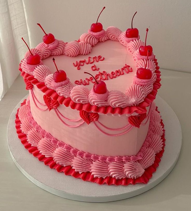 a heart shaped birthday cake with cherries and hearts on the top is sitting on a table