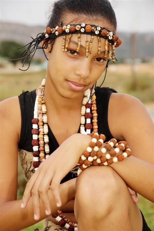 a woman with beads on her head sitting in the grass