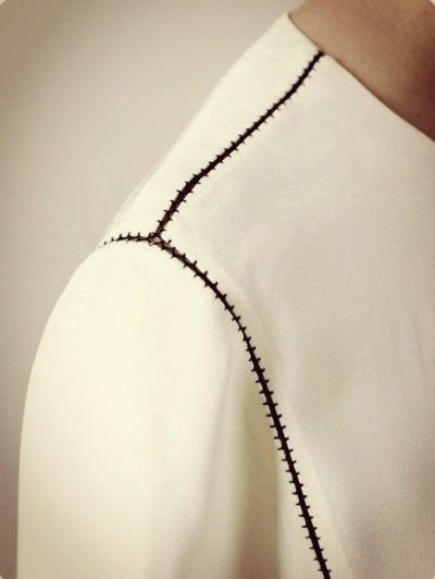 the back of a woman's white top with black stitching