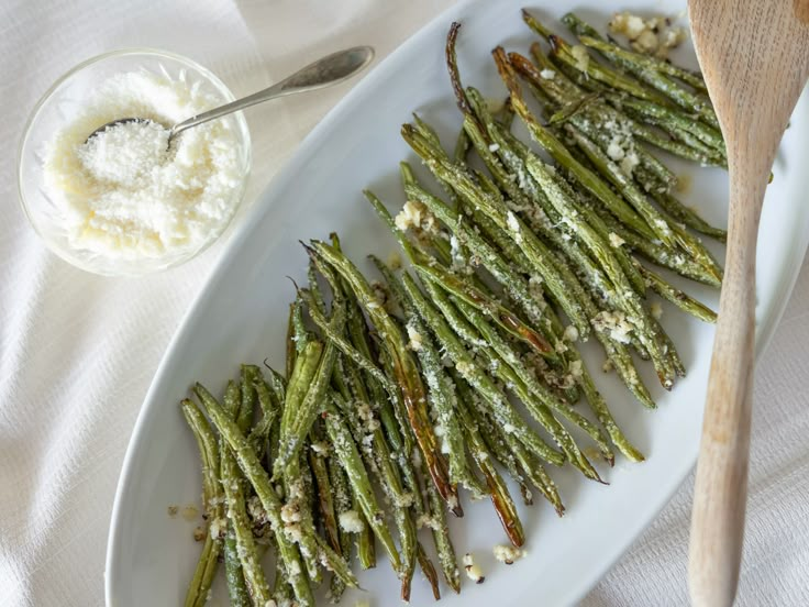 cooked green beans with parmesan cheese on a white platter next to a wooden spoon