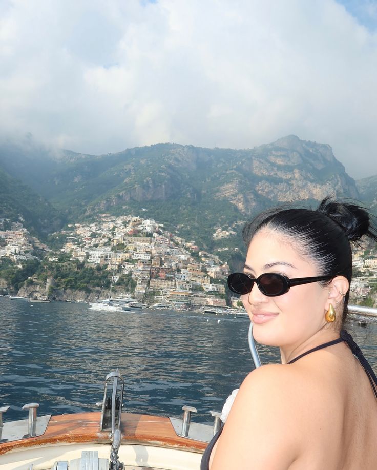 a woman sitting on the back of a boat in front of a city and mountains