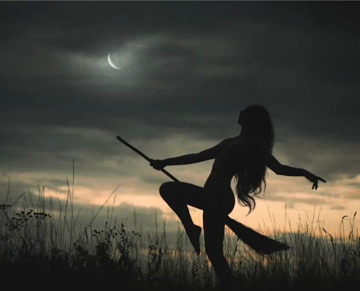 a woman is holding a broom in the air while standing on a hill at night