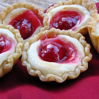 four small pies with jelly filling on them sitting on a red cloth covered table